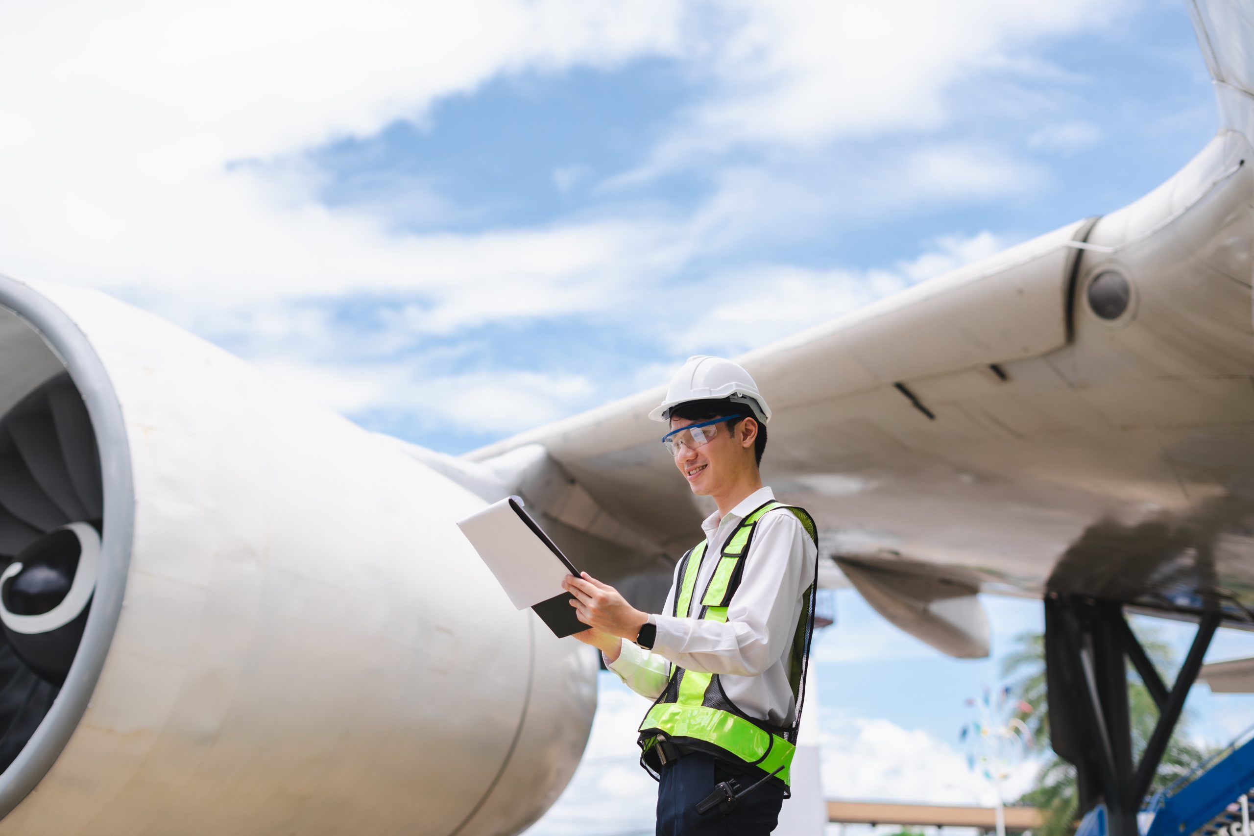 Male engineer in white hardhat standing and holding tablet worki